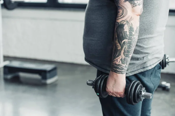 Cropped view of Overweight tattooed man training with dumbbells at sports center with copy space — Stock Photo