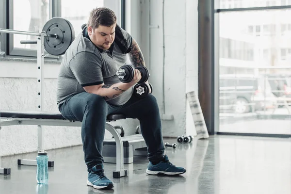 Übergewichtiger tätowierter Mann trainiert mit Kurzhanteln im Fitnessstudio mit Kopierraum — Stockfoto