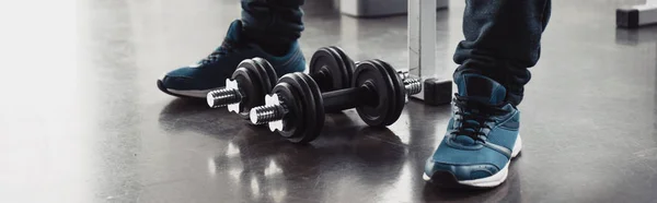 Panoramic shot of man in trainers sitting with dumbbells at sports center — Stock Photo