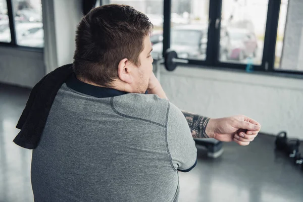 Rückenansicht eines übergewichtigen tätowierten Mannes mit Handtuchstrecken im Fitnessstudio — Stockfoto