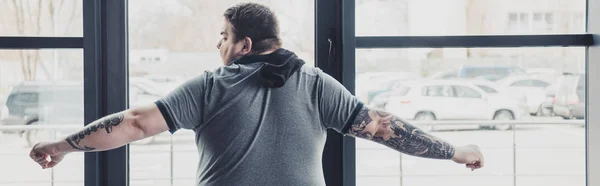 Vista posterior del hombre tatuado con sobrepeso en camiseta gris estirándose en el gimnasio - foto de stock