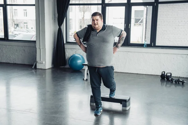 Надмірна вага чоловіка в сірій футболці з рушником тренування на кроковій платформі спортивного центру — стокове фото