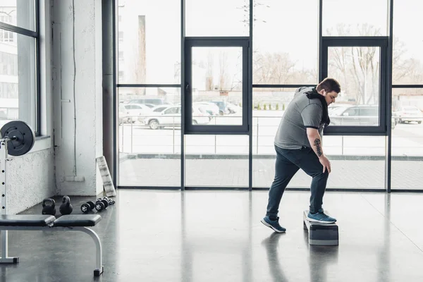 Человек с избыточным весом с полотенцем тренировки на ступенчатой площадке в спортивном центре с копировальным пространством — стоковое фото