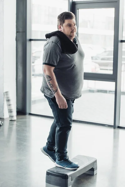 Overweight man with towel training on step platform at gym — Stock Photo