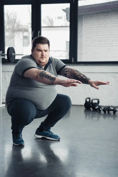 Übergewichtiger tätowierter Mann macht Kniebeugen im Sportzentrum — Stockfoto