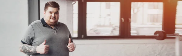 Panoramic shot of overweight tattooed man Looking At Camera and showing thumbs up at gym with copy space — Stock Photo