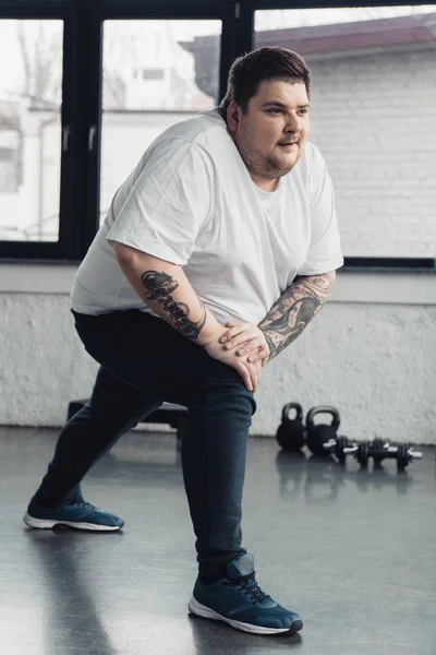 Sobrepeso tatuado homem alongamento pernas no esportes centro — Fotografia de Stock
