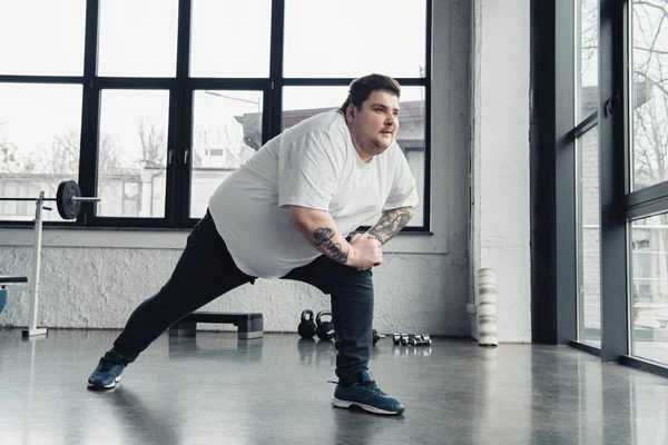 Overweight tattooed man stretching legs at sports center — Stock Photo