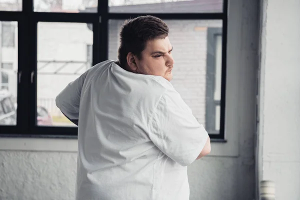 Sovrappeso tatuato uomo in bianco t-shirt che si estende in palestra — Foto stock