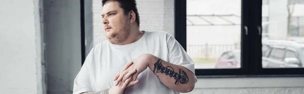 Панорамный снимок человека с татуировкой с избыточным весом, растягивающего пальцы в спортзале — стоковое фото