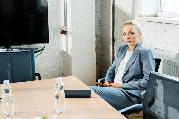 Attraktive blonde Businesstrainerin sitzt im Konferenzraum und blickt in die Kamera — Stockfoto