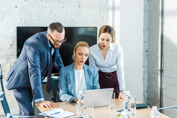 Handsome man in glasses near attractive businesswomen looking at laptop — Stock Photo