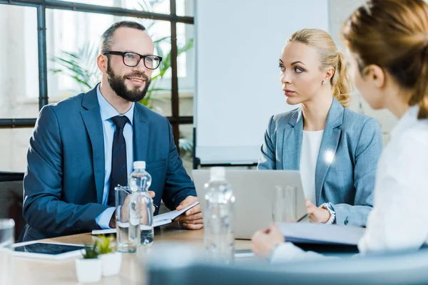 Alegre hombre de negocios sentado con atractivas empresarias en la sala de conferencias - foto de stock