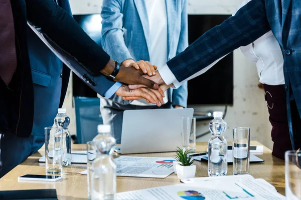 Abgeschnittene Ansicht multikultureller Männer und Frauen, die ihre Hände in der Nähe von Diagrammen und Grafiken zusammenlegen — Stockfoto