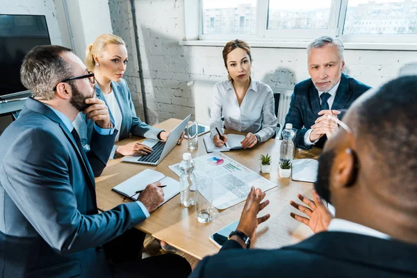 Enfoque selectivo de las mujeres de negocios mirando a su compañero de trabajo afroamericano en la sala de conferencias - foto de stock