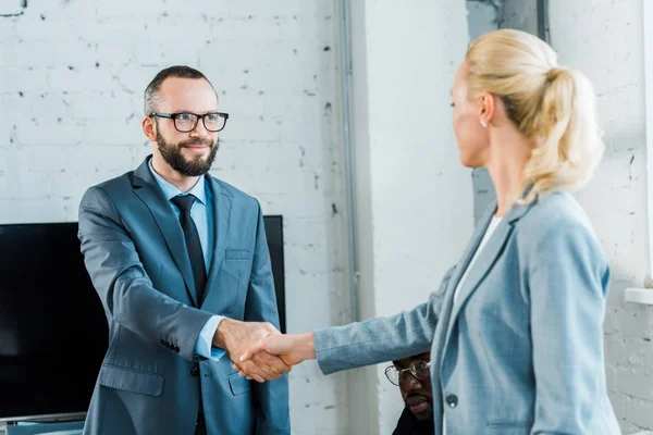 Guapo hombre de negocios en gafas estrechando la mano con rubia mujer de negocios - foto de stock