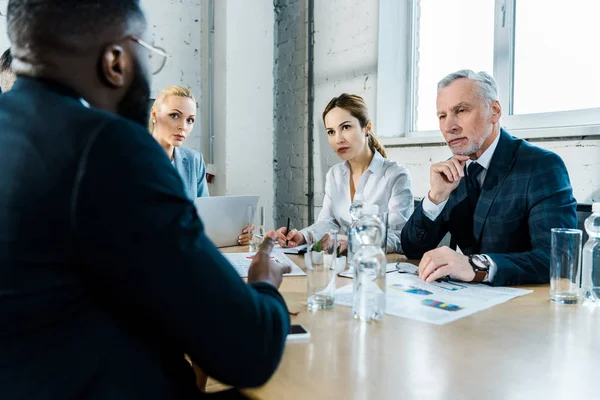 Donne d'affari e uomo d'affari guardando collaboratore afro-americano in sala conferenze — Foto stock