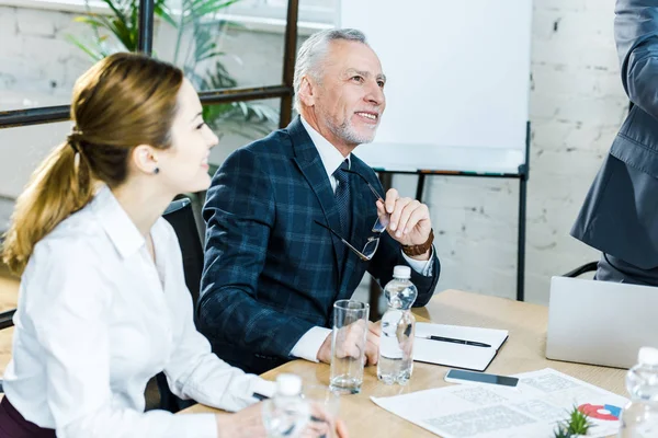 Hombre de negocios guapo y alegre sentado con atractiva mujer de negocios en la sala de conferencias - foto de stock