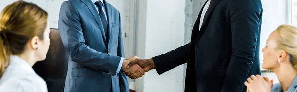 Plan panoramique d'hommes d'affaires multiculturels serrant la main près de collègues au bureau — Photo de stock