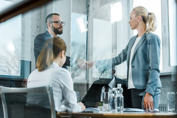 Handsome bearded  business coach shaking hands with blonde woman near multicultural coworkers — Stock Photo