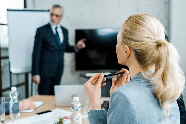 Foyer sélectif de femme d'affaires blonde tenant stylo tout en regardant entraîneur d'affaires — Photo de stock