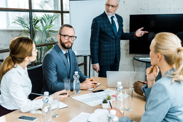 Business coach che punta con dito vicino alla tv con schermo bianco e persone multiculturali — Foto stock