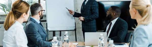 Colpo panoramico di business coach che punta sulla lavagna bianca con penna vicino a colleghi multiculturali — Foto stock
