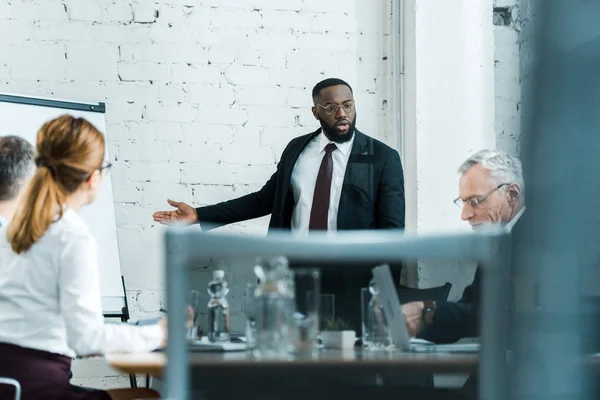 Selektiver Fokus eines afrikanisch-amerikanischen Business Coaches in Brille, der in der Nähe von Mitarbeitern gestikuliert — Stockfoto