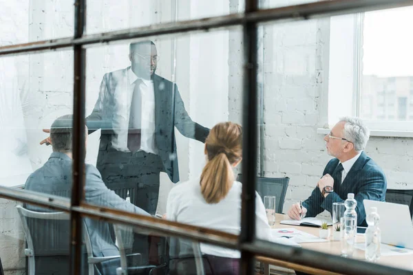 Enfoque selectivo del entrenador de negocios afroamericano hablando y haciendo gestos cerca de compañeros de trabajo - foto de stock