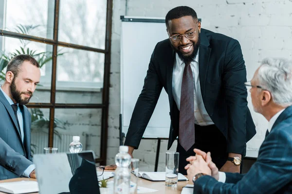 Foco seletivo de alegre treinador de negócios afro-americano sorrindo perto de colegas de trabalho — Fotografia de Stock