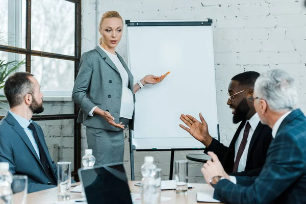 Schwangere blonde Businesstrainerin steht neben Whiteboard und gestikuliert im Konferenzraum — Stockfoto