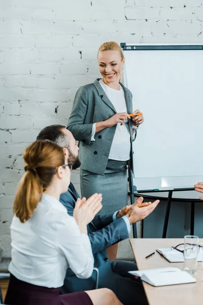 Selective focus of happy pregnant business coach standing while coworkers clapping hands — Stock Photo