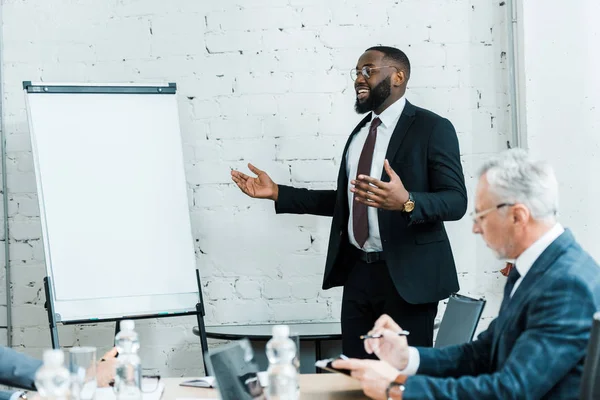 Happy african american business coach talking near white board and colleague — Stock Photo