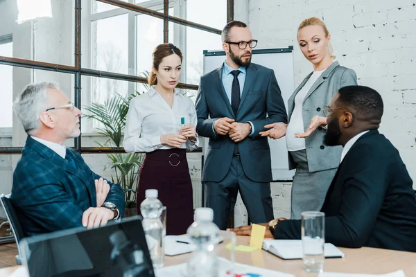 Enfoque selectivo de la mujer de negocios embarazada de pie cerca de compañeros de trabajo multiculturales - foto de stock