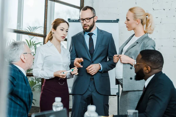 Foyer sélectif de l'homme d'affaires parlant et pointant du doigt près de collègues multiculturels et femme blonde enceinte — Photo de stock