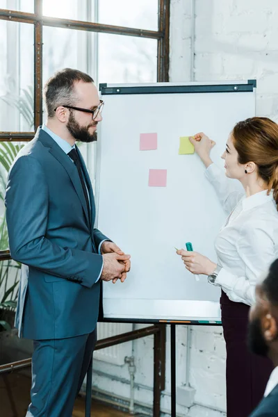 Selektiver Fokus des Geschäftsmannes auf Geschäftsfrau, die neben Whiteboard mit klebrigen Zetteln steht — Stockfoto