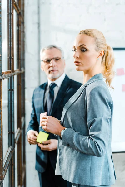 Selective focus of attractive blonde woman holding sticky note near businessman — Stock Photo
