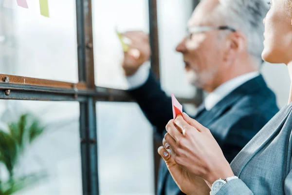 Foyer sélectif de femme d'affaires regardant homme d'affaires mettant note collante sur la fenêtre — Photo de stock