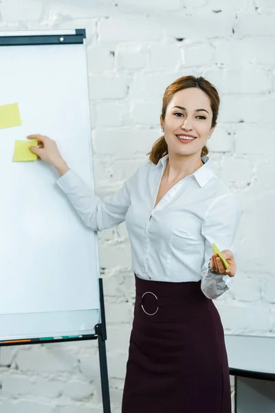 Cheerful business coach putting sticky notes on white board — Stock Photo