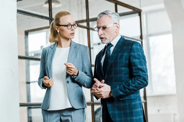 Barbudo hombre de negocios hablando con atractiva mujer de negocios rubia - foto de stock