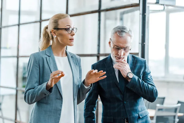 Attraktive blonde Geschäftsfrau gestikuliert im Gespräch mit bärtigen Geschäftsmann — Stockfoto