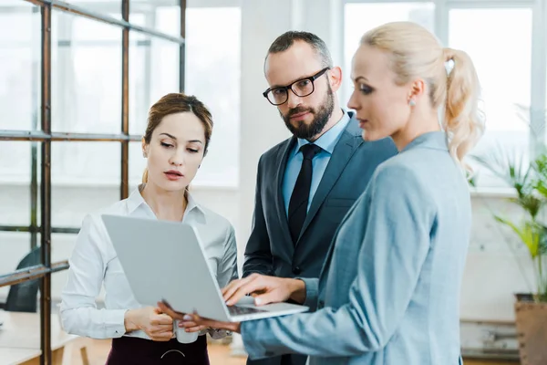 Selective focus of handsome businessman standing near blonde woman holding laptop — Stock Photo