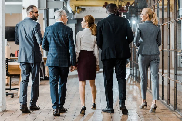 Back view of multicultural group of businessmen and businesswomen walking in office — Stock Photo