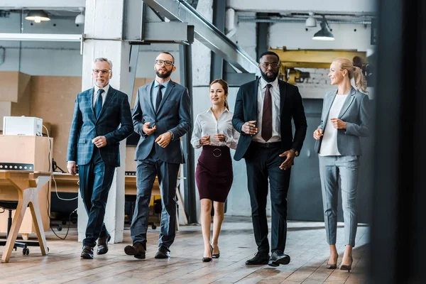 Multicultural group of handsome businessmen and cheerful businesswomen walking in office — Stock Photo