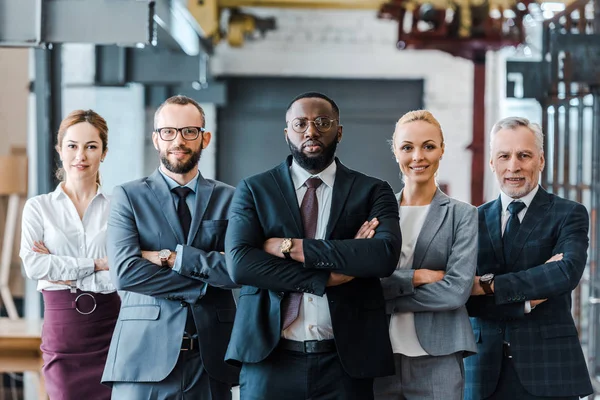 Grupo multicultural de hombres de negocios guapos y mujeres de negocios alegres de pie con los brazos cruzados y mirando la cámara - foto de stock