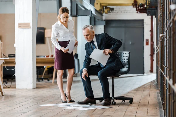 Hombre de negocios barbudo señalando con el dedo los gráficos y gráficos mientras está sentado en la silla cerca de la mujer de negocios - foto de stock