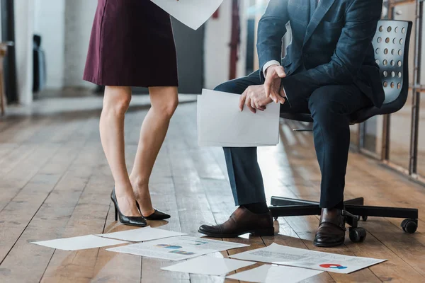 Abgeschnittene Ansicht eines Geschäftsmannes, der leeres Papier in der Nähe einer Geschäftsfrau hält, während er auf einem Stuhl sitzt — Stockfoto