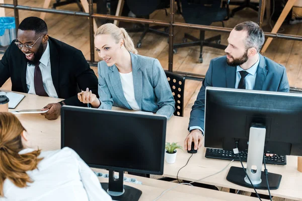 Attractive businesswoman gesturing and talking with multicultural coworkers — Stock Photo