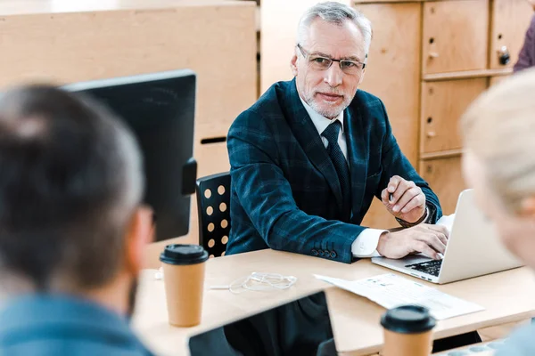 Foco seletivo do homem de negócios em óculos olhando para colegas de trabalho no escritório — Fotografia de Stock