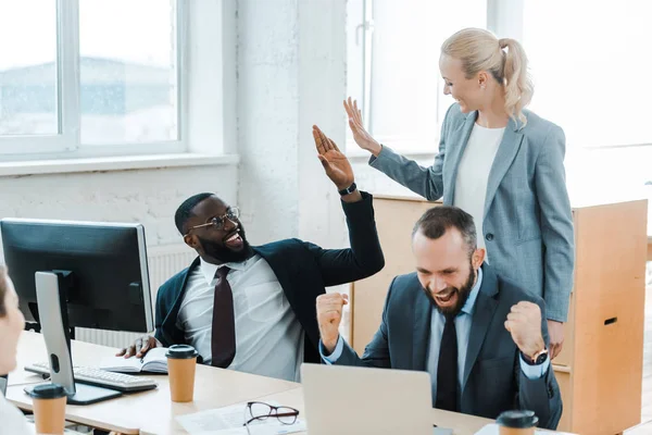 Fröhliche Geschäftsfrau gibt afrikanisch-amerikanischen Geschäftsmann in der Nähe von Mitarbeitern High Five — Stockfoto